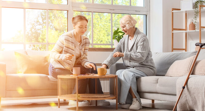 Elderly care and home assistance, young caregiver helping senior woman with daily activities and social support in a bright living room at home
