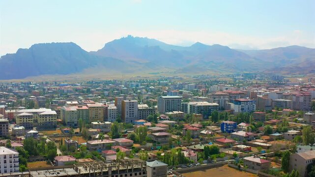 Drone hovers above central Dogubayazit with surrounding mountains, low rise districts and commercial blocks, supporting city overview, urban development, tourism media and regional geography in Turkey