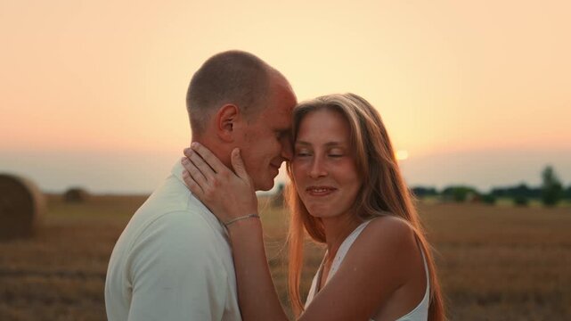 Smiling couple embracing affectionately in a golden field at sunset, sharing a tender intimate moment together with warm soft light and serene romantic atmosphere