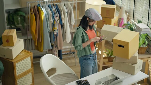 Starting SME Small business entrepreneur,Online business, Work at home concept.Asian business woman using a laptop computer and phone call receive checking customer order online shipping boxes at home