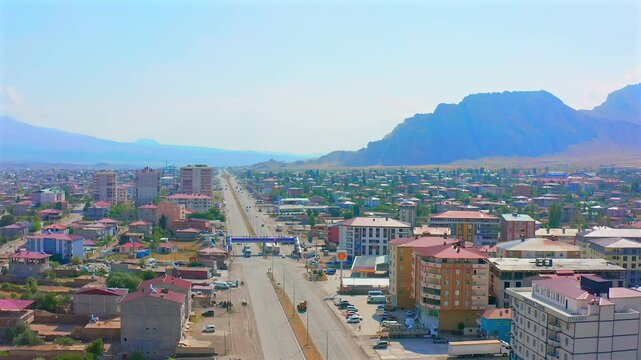 Drone flies forward above a broad city boulevard toward rugged mountains in eastern Turkey, showing traffic, housing and urban expansion for transport planning, tourism and regional geography media.
