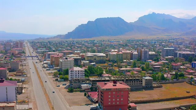 Drone flies forward above Dogubayazit urban corridor with a straight avenue, apartment buildings and rocky mountains, supporting transport planning, city growth, tourism promotion and Turkey geography