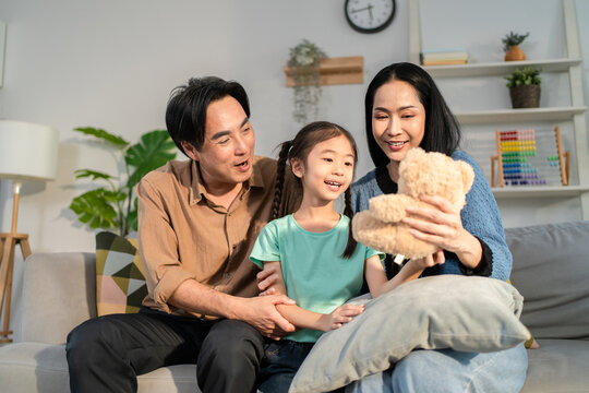 Asian loving mother and father giving a teddy bear to young daughter.