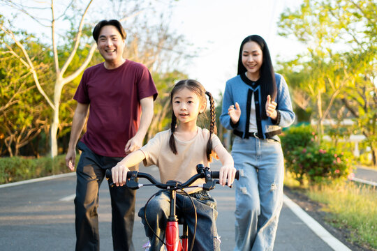 Asian young girl riding bicycle in garden while her parents look after. 