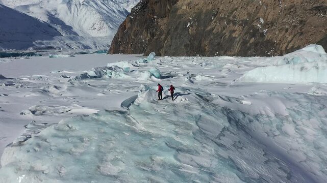 Aerial view of two hikers trekking across a vast glacier in Tibet