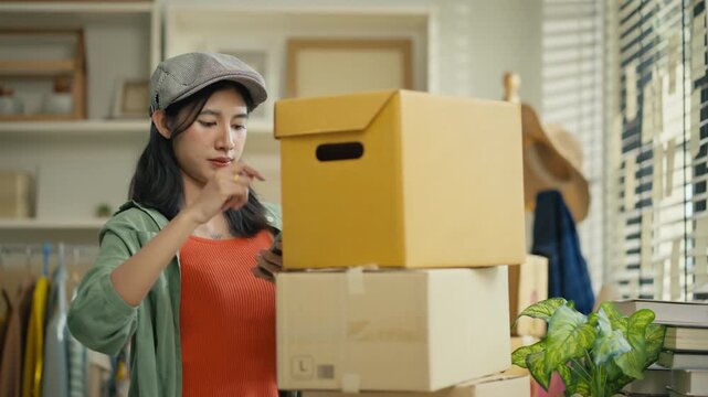 Starting SME Small business entrepreneur,Online business, Work at home concept.Asian business woman using a laptop computer and phone call receive checking customer order online shipping boxes at home