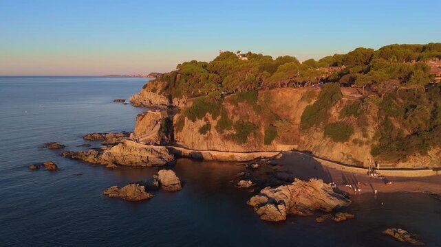 Aerial view taken from a drone of the coast of Lloret de Mar, Costa Brava, Spain, early in the morning at sunrise - the sea, beach and coastal cliffs of the city bay