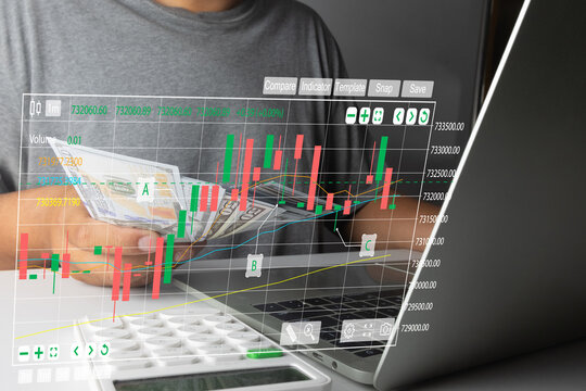 Man holding US dollar prop money with digital candlestick chart overlay while using a laptop. Concept of day trading, cryptocurrency investment, forex market, and financial success.