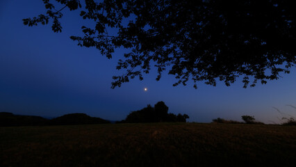 Moon on a twilight sky with stars, planets and landscape mountain silhouettes. © astrosystem