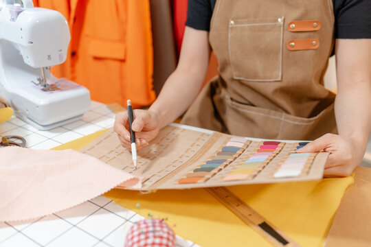 Professional fashion designer selecting fabric swatches, thread colors and sewing supplies in a modern studio. Creative textile design, apparel development and garment production.