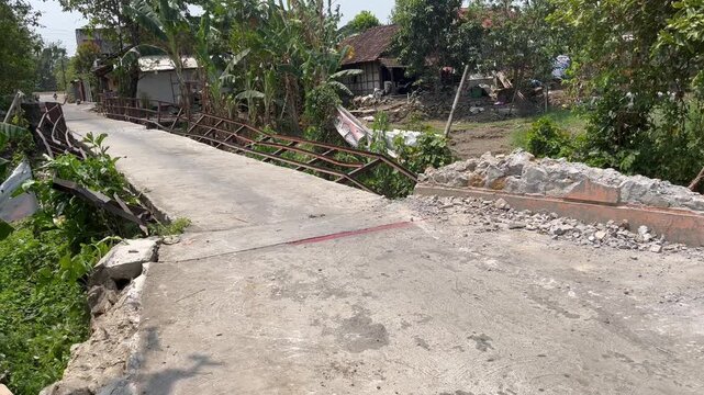 Collapsed road and broken bridge railing in rural village