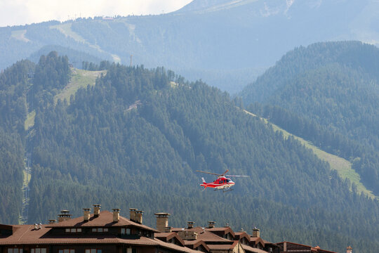Bansko, Bulgaria, red emergency medical service helicopter flying over town, green Pirin mountains