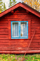Red log cabin with blue window frame in autumn forest © Lars Johansson