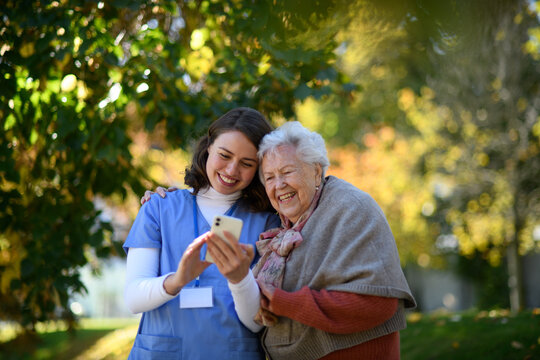 Portrait of nurse and elderly woman on walk in the park during warm autumn day.
