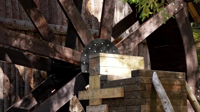 Sunlight dances on a historic oak mill wheel, turning rhythmically in a quiet forest creek on a peaceful summer morning.