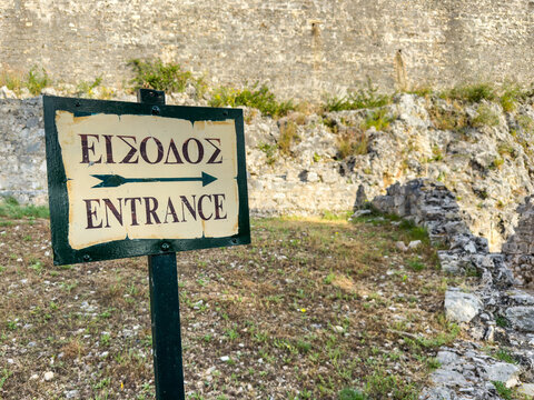 Bilingual entrance sign at weathered stone ruins, New Fortress, Corfu Town, Greece