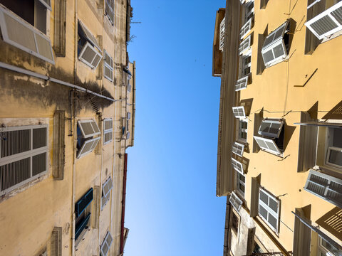Yellow traditional buildings with white shutters over narrow old town alley, Corfu, Greece
