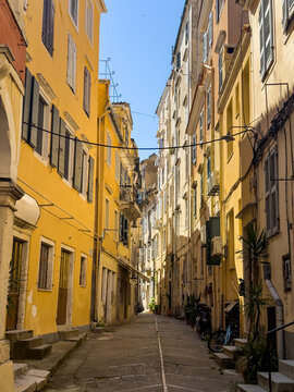 Narrow stone alley, Corfu Old Town, Greece, lined by yellow buildings and potted plants