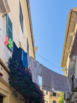 Colorful laundry hangs between shuttered traditional buildings over a narrow alley in Corfu Old Town, Greece, blue sky