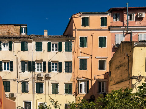 Pastel apartment facades with green shutters and tiled roofs in Corfu Old Town, Greece