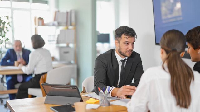 Adult male bank employee at desk with laptop and discussing with young couple customers 
