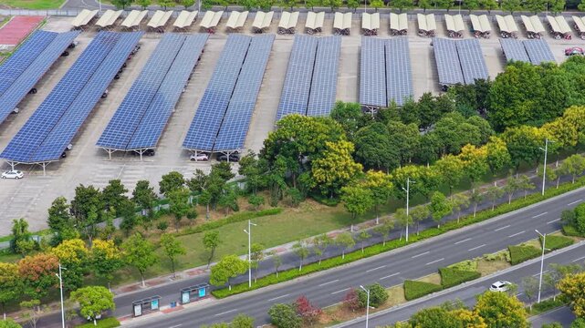 Aerial tracking view of solar carports beside a tree lined road