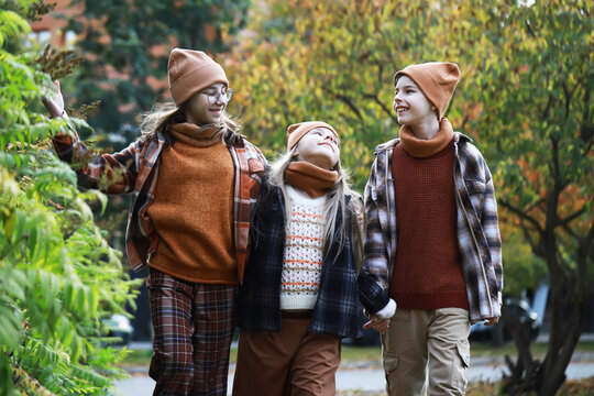 Smiling Siblings in Autumn Outfits Enjoying a Stroll Through a Leafy Park