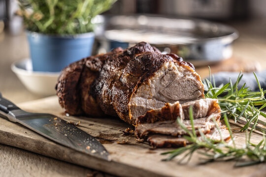 Tasty roasted pork neck with a crispy crust is garnished with fresh rosemary and sliced on a wooden board. 