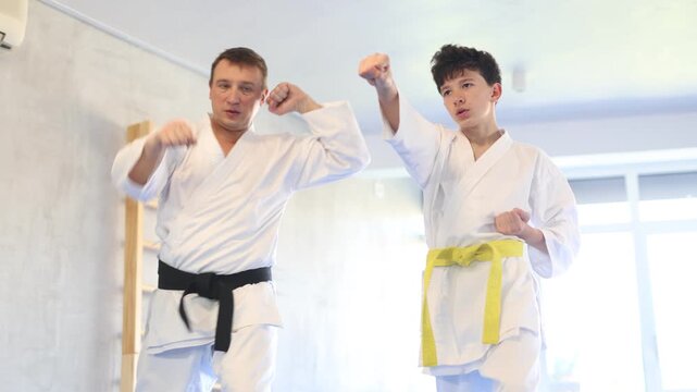 Adult man and boy teen karatekas train karate technique in studio 