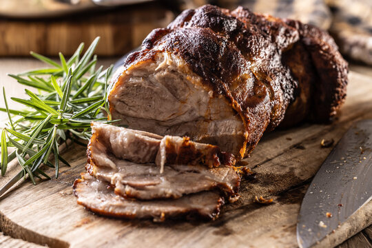 Tasty roasted pork neck with a crispy crust is garnished with fresh rosemary and sliced on a wooden board. 