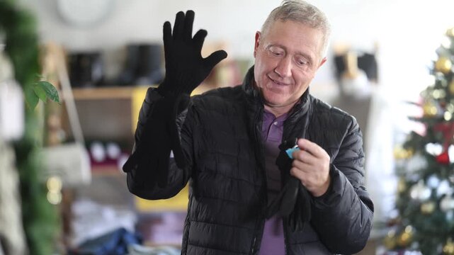 Attentive mature man choosing some jeans pantaloons during Christmas sale in clothing shop . High quality 4k footage