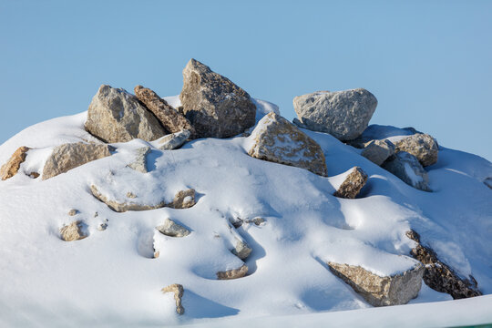 Snow blankets rocky outcrop under clear blue sky. Large, jagged stones protrude from white snow cover.