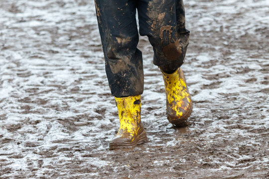 Sturdy yellow boots caked in mud and rainwater, standing on a soggy