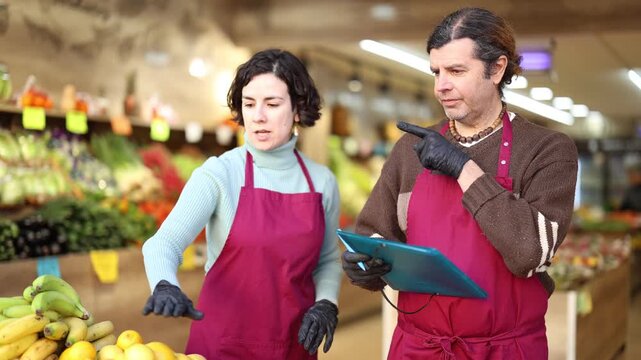 Adult man and woman sellers conducting inventory with checklist in vegetable shop 