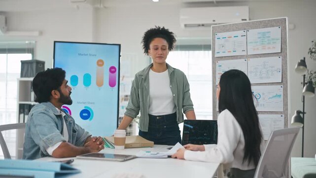 Professional businesswoman standing in front of a large display, explaining market share pie charts and business analytics to her team.