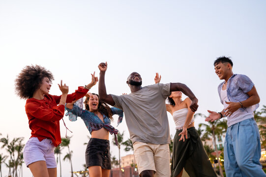 Joyful summer beach party with multiethnic friends celebrating vacation, enjoying music, freedom