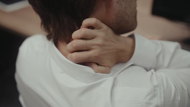Fatigued businessman massaging painful neck and stiff shoulders, suffering from body ache after long day of sedentary work in office, indicating burnout and physical discomfort, close-up, slow motion.