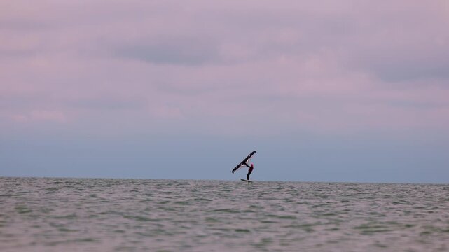 An athlete standing on the board holds on to the wing, in which the wind creates thrust in slow motion. Wingfoil board where a surfer glides through the water on a hydrofoil board..