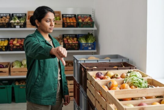 Woman employee checking for rotten fruit and vegetables, indicating food waste