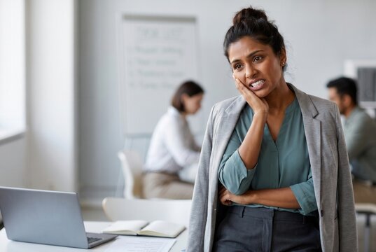 Woman experiencing severe tooth pain while working in a modern office environment