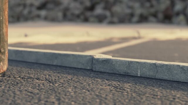 The scene shows a parking lot with asphalt and concrete edges. The ground appears worn and shows signs of use. There are small pebbles scattered nearby, indicating outdoor exposure.