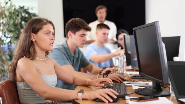 Positive interested young girl using computer to surf internet in busy library, searching educational resources and materials during self-study 