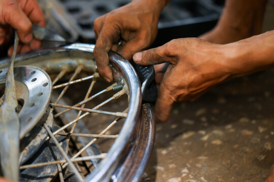 Motorcycle wheel repair mechanic hand adjusting metal spoke and rim inside workshop with grease, tool, close up detail, maintenance service focus