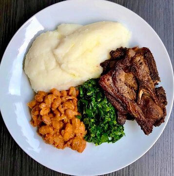 Traditional Zambian nshima made from maize meal, served as a staple food with vegetables and savory side dishes. Authentic African cuisine presented on a plate.