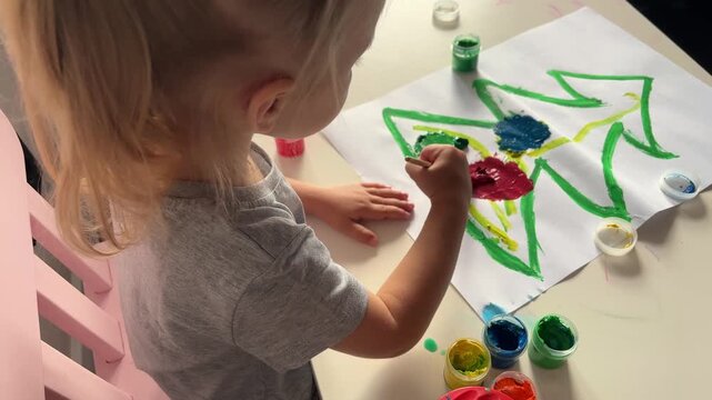Young girl paints a Christmas tree with colorful gouache at a table, festive craft, creative childhood, holiday activity, Christmas.