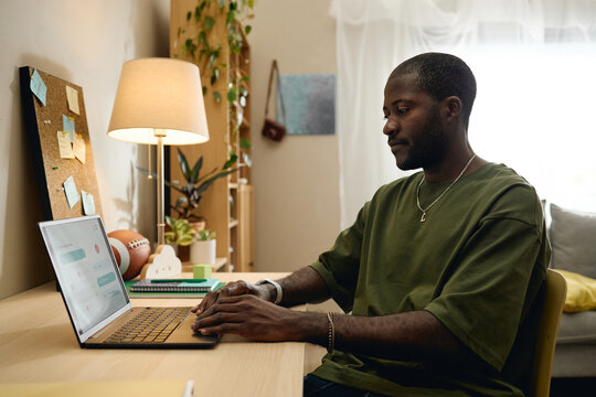 African American young adult man typing on laptop keyboard organizing schedule at desk. Visual suitable for remote work, digital productivity apps, online education marketing