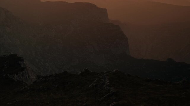 The scene shows mountains in the distance as the sun sets, casting shadows. The landscape is rocky with a dark atmosphere. Colors blend softly in the sky above.