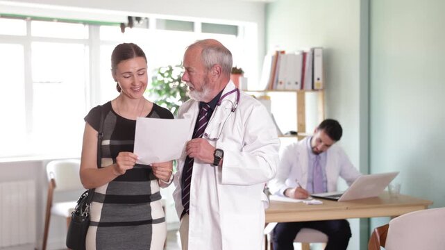 Senior male doctor and woman patient examine papers, discuss medical tests result. Specialist interprets tests, tells you action plan to achieve goals of treatment. 