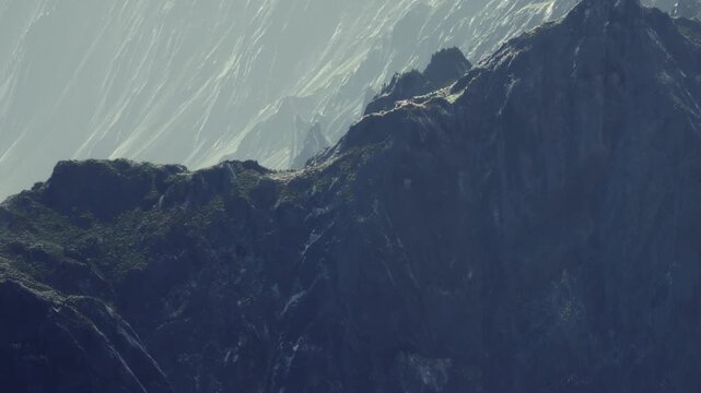 A mountain with rugged surfaces in the foreground. Bright light hits the distant slopes. The image captures the natural shapes and textures of the rocks.