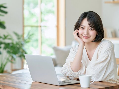 窓際で笑顔で頬に手を添えリラックスしてノートPCに向かう女性